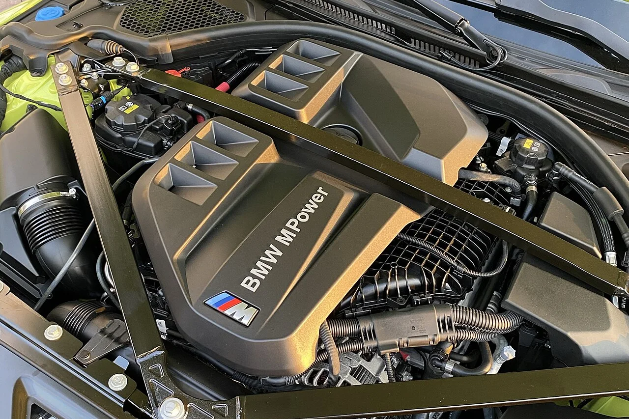 Engine bay of a BMW M3 Competition showing the S58 engine cover and the strut tower bracing above it