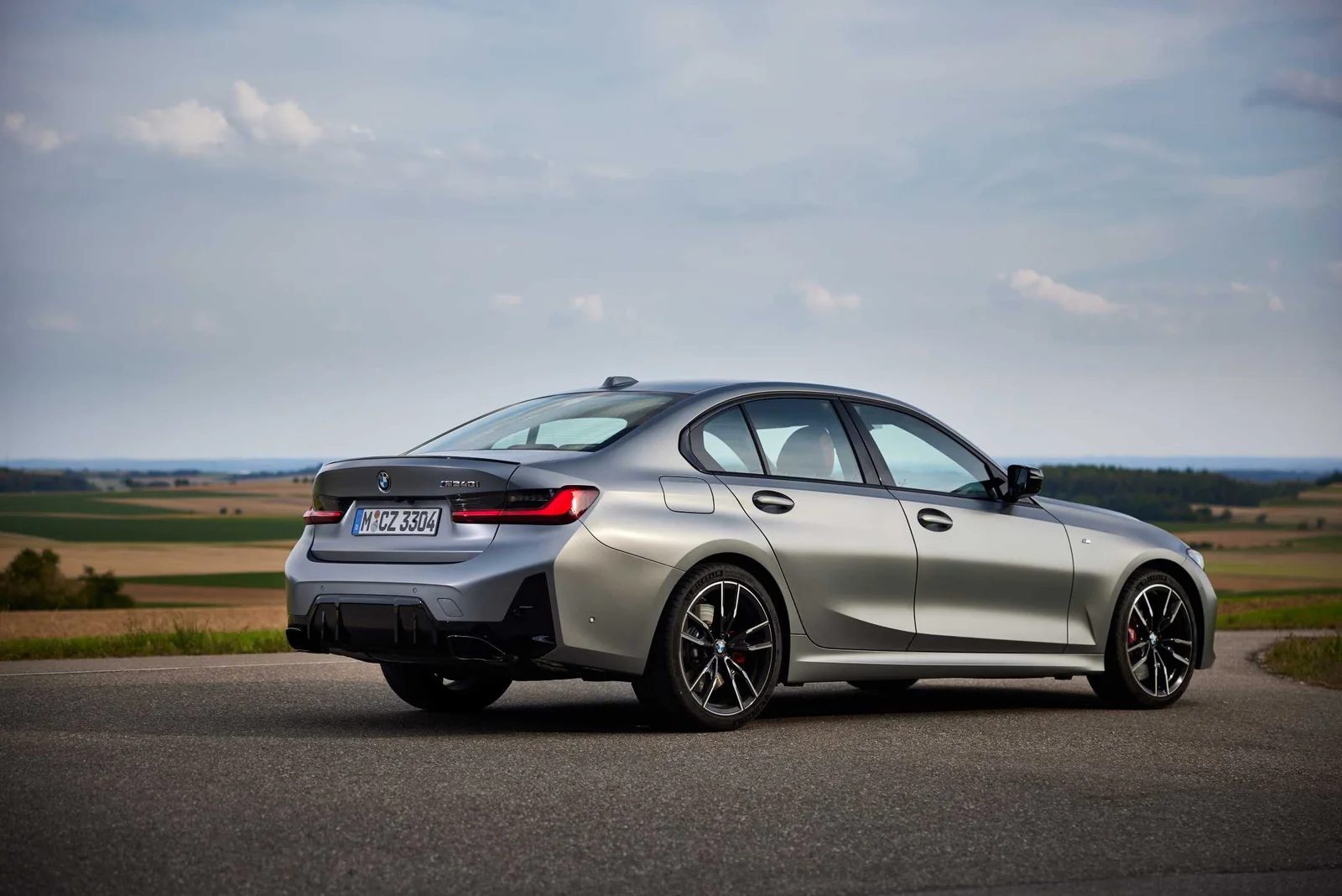 Grey BMW M340i xDrive sedan parked on a country road, rear three-quarter view showing its exhaust tips