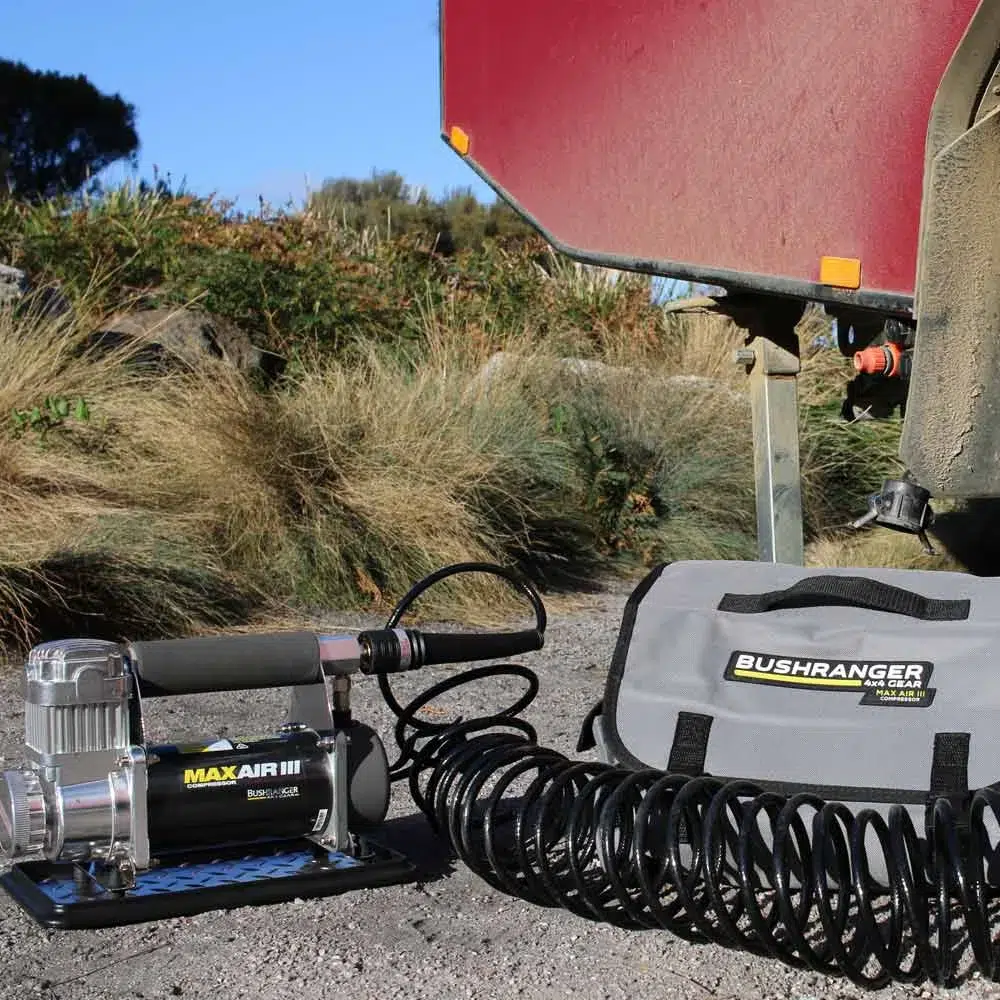 Bushranger Max Air III portable compressor with coiled air hose sitting on sand beside a 4WD wheel