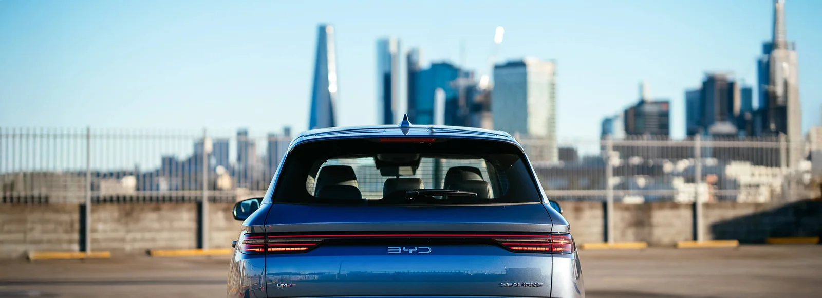 Rear view of a blue BYD Sealion 5 plug-in hybrid SUV parked in front of a city skyline