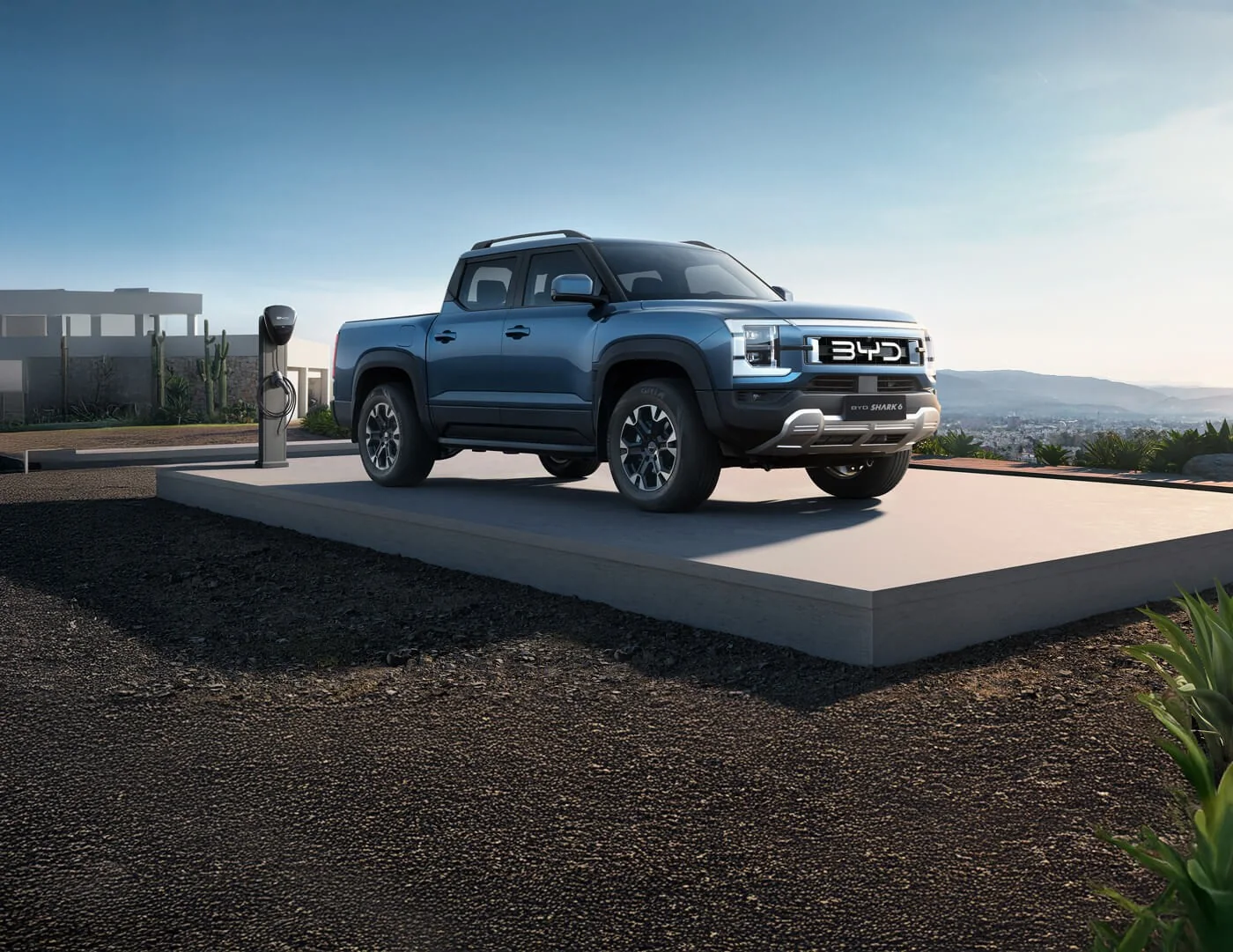 Blue BYD Shark 6 plug-in hybrid ute parked on a concrete pad next to an electric vehicle charger