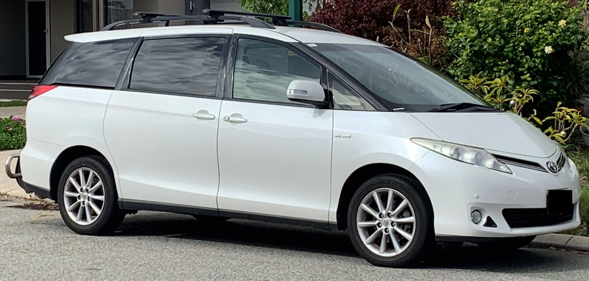 White Toyota Tarago people mover with clear front door glass and dark factory privacy glass on the rear windows