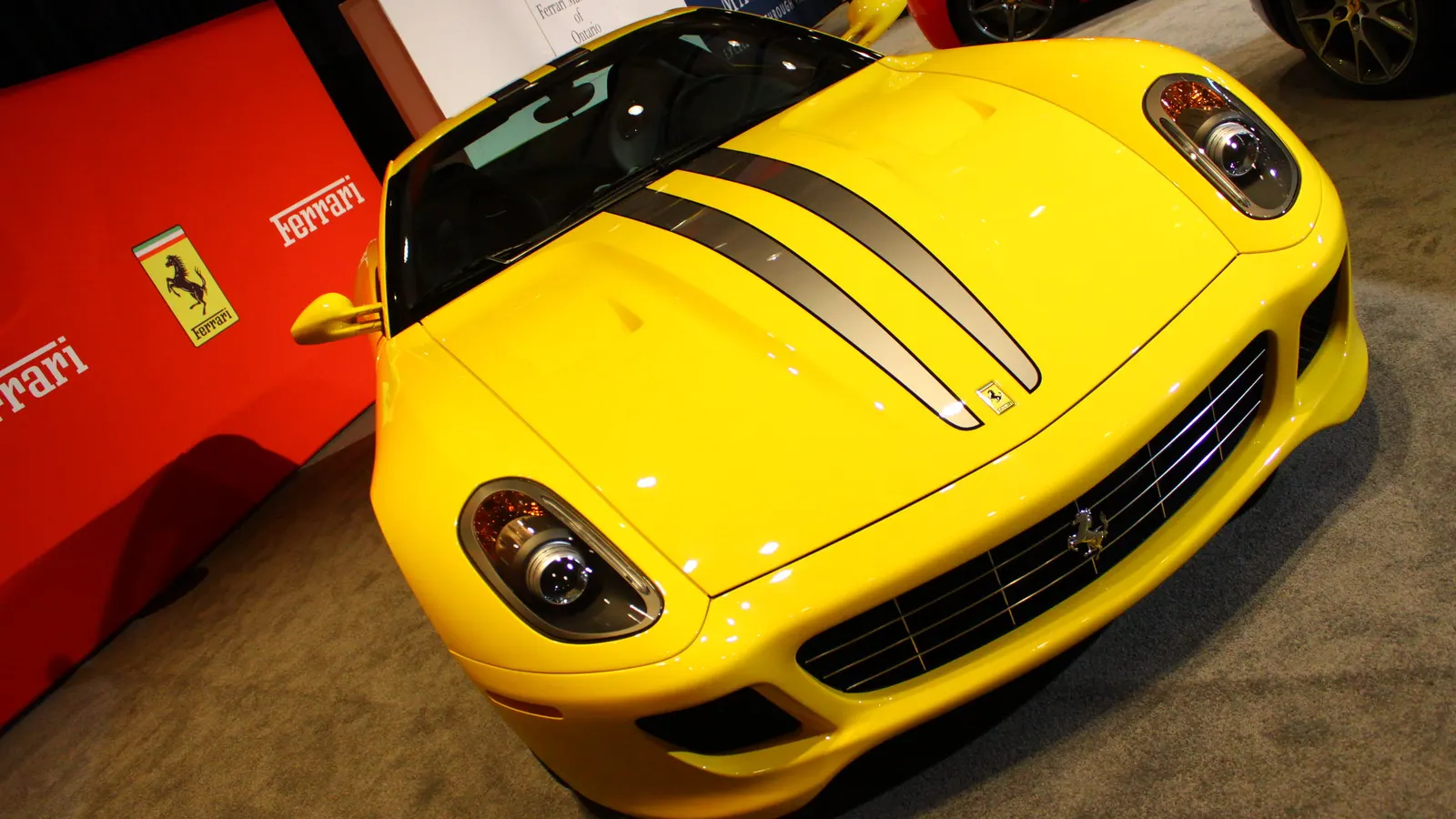 Yellow Ferrari 599 GTB Fiorano with grey racing stripes on display, showing its headlights and grille