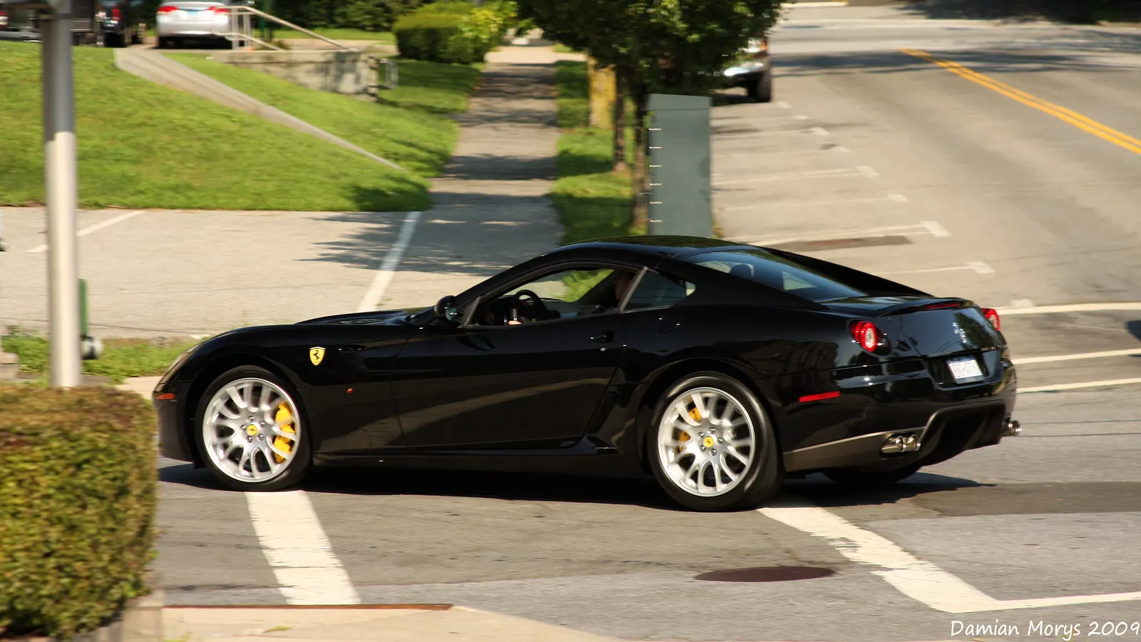 Side profile of a black Ferrari 599 GTB Fiorano with silver wheels and yellow brake calipers on a suburban street