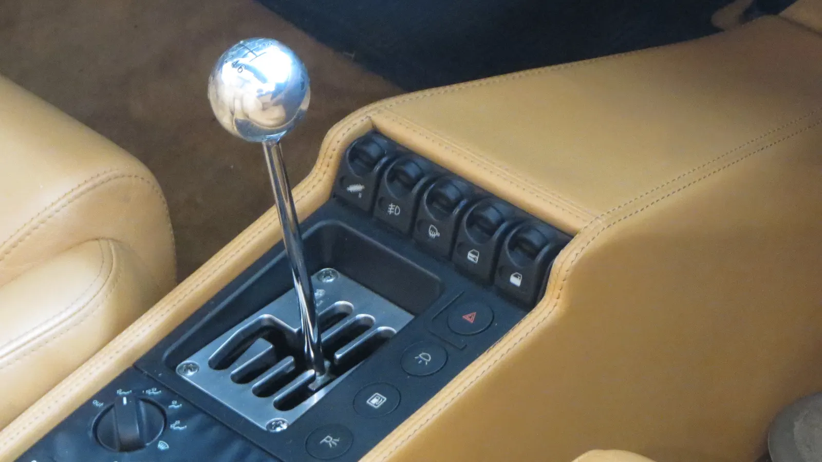 Chromed gear knob and lever in a polished open metal gate on the tan leather console of a manual Ferrari