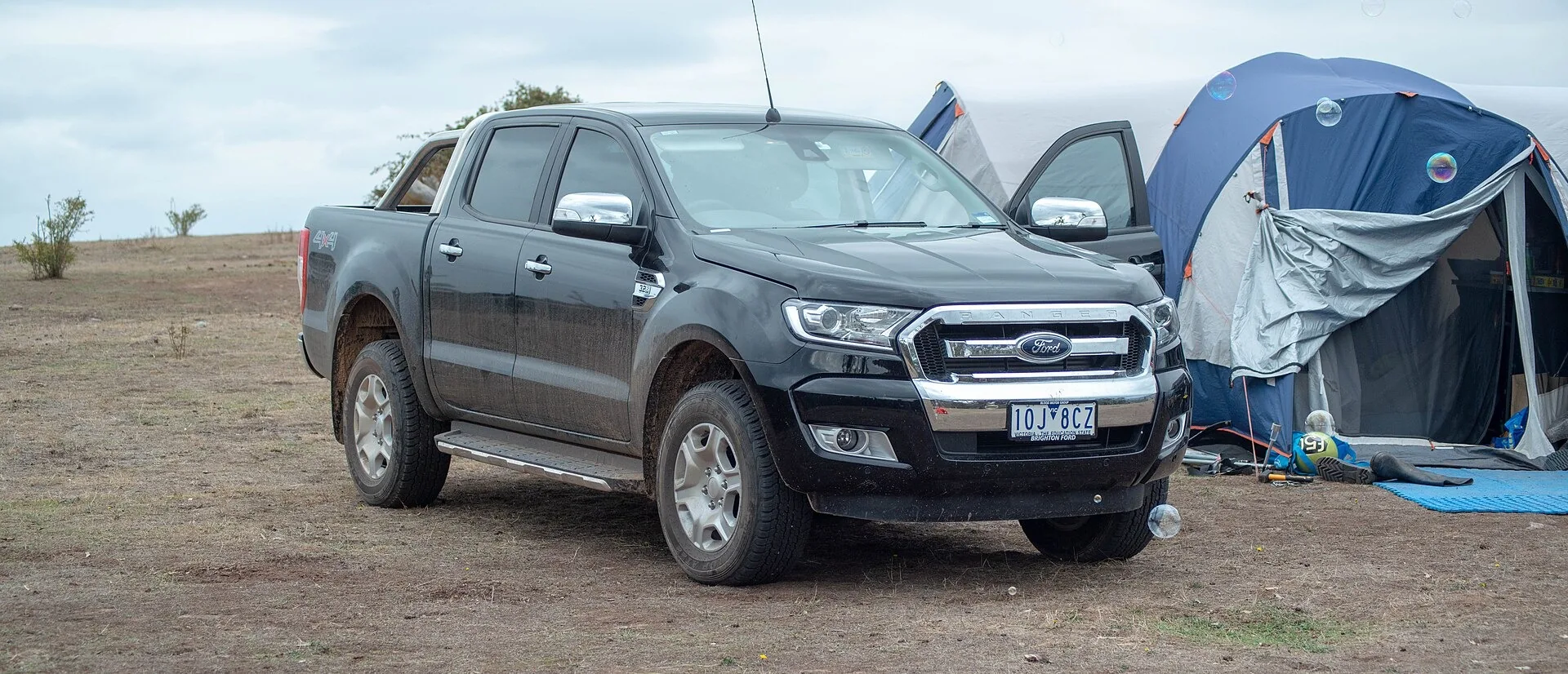 Black Victorian-registered PX Ford Ranger dual-cab ute parked beside a tent at a dry campsite