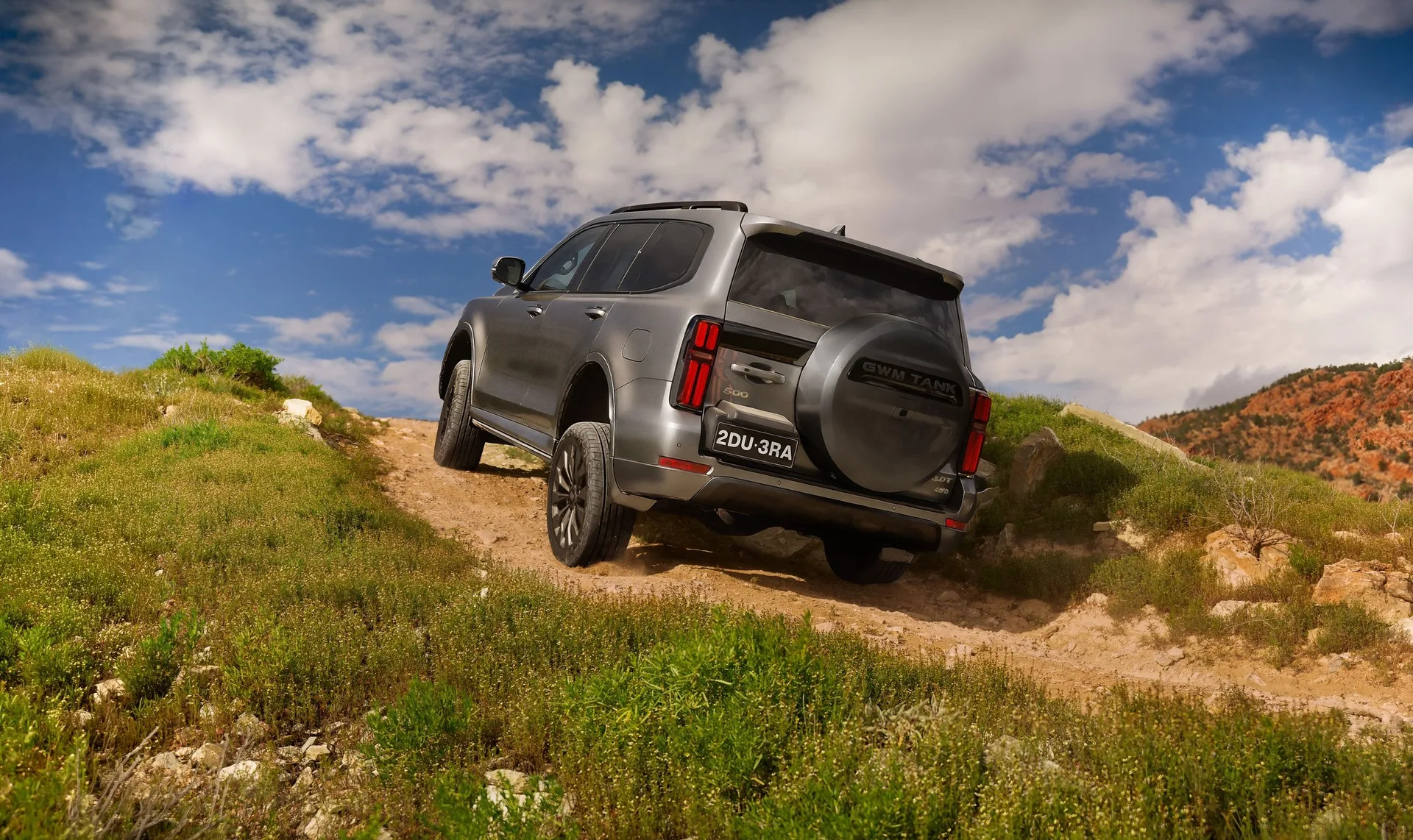 GWM Tank 500 diesel climbing a grassy hill track, rear three-quarter view with spare wheel on the tailgate