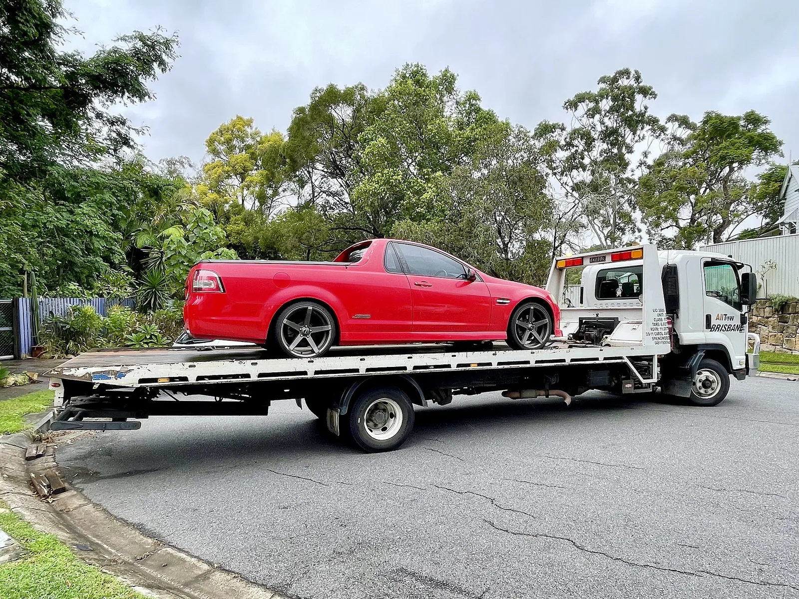 Red Holden SS ute loaded on a tilt-tray tow truck on a suburban street in Brisbane
