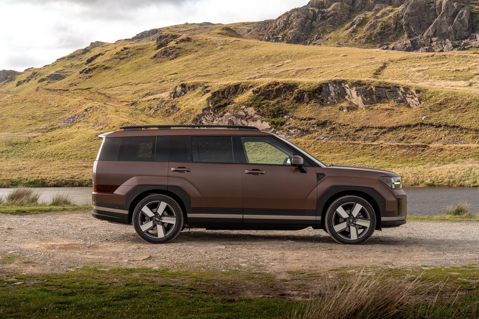 Bronze Hyundai Santa Fe in side profile showing its boxy, upright body and long wheelbase beside a lake