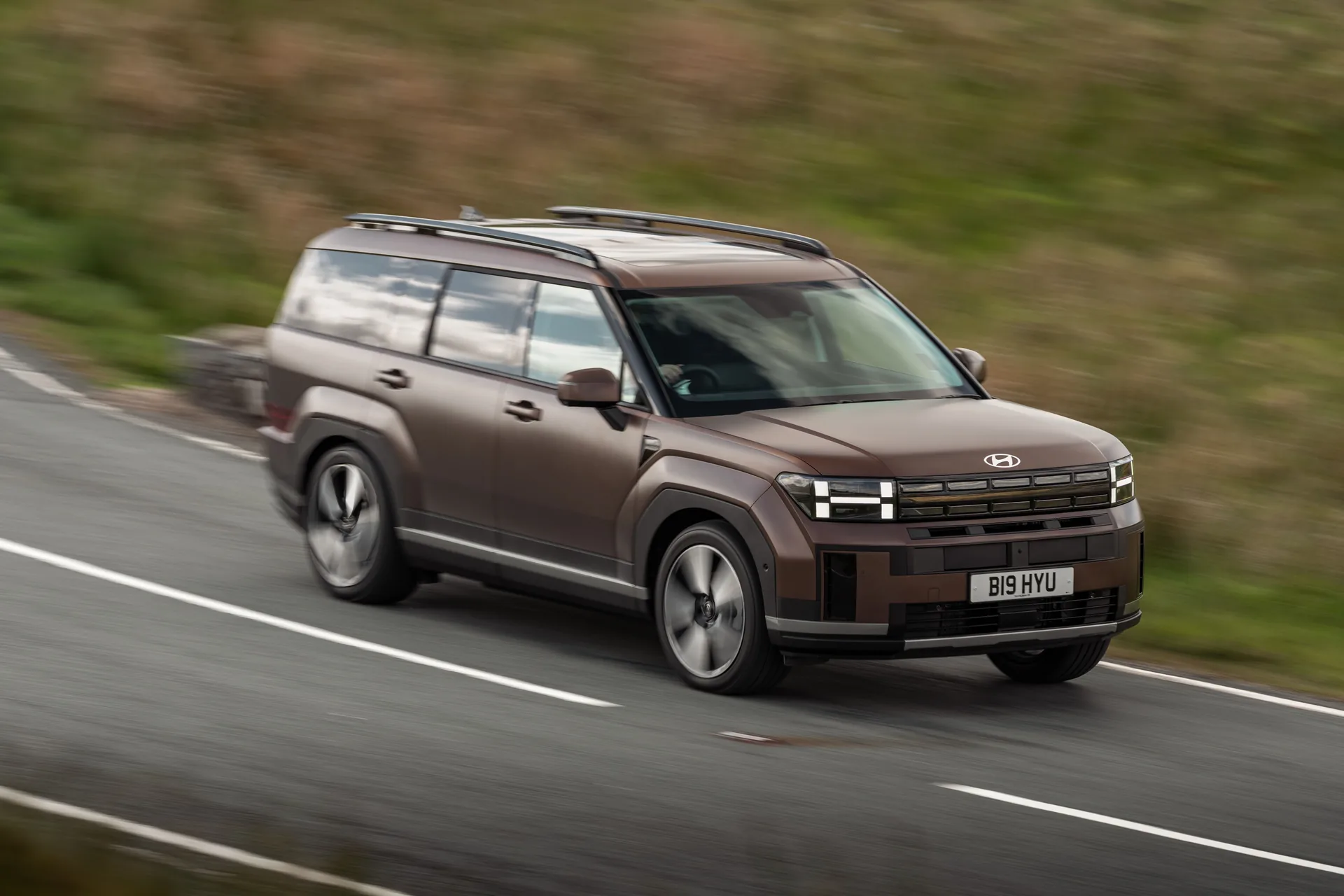Bronze Hyundai Santa Fe driving along a country road, front three-quarter view with motion blur