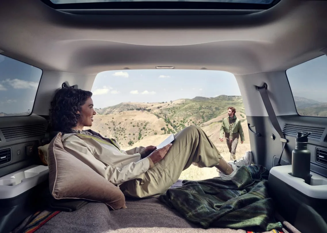 Passenger relaxing in the Hyundai Santa Fe cargo area with the wide tailgate open to a mountain view