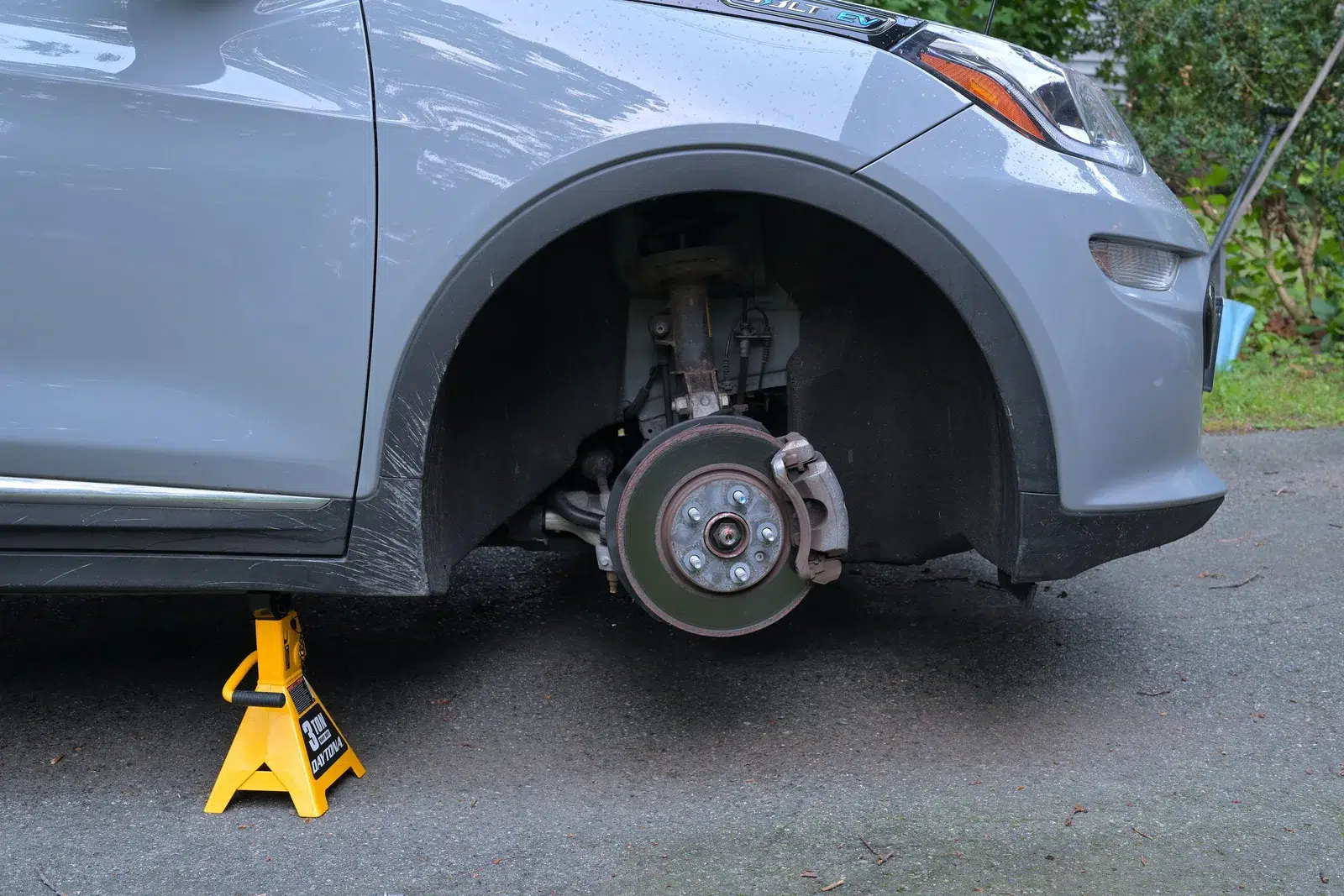 Yellow jack stand placed under the body beside a front wheel arch with the wheel removed and brake exposed