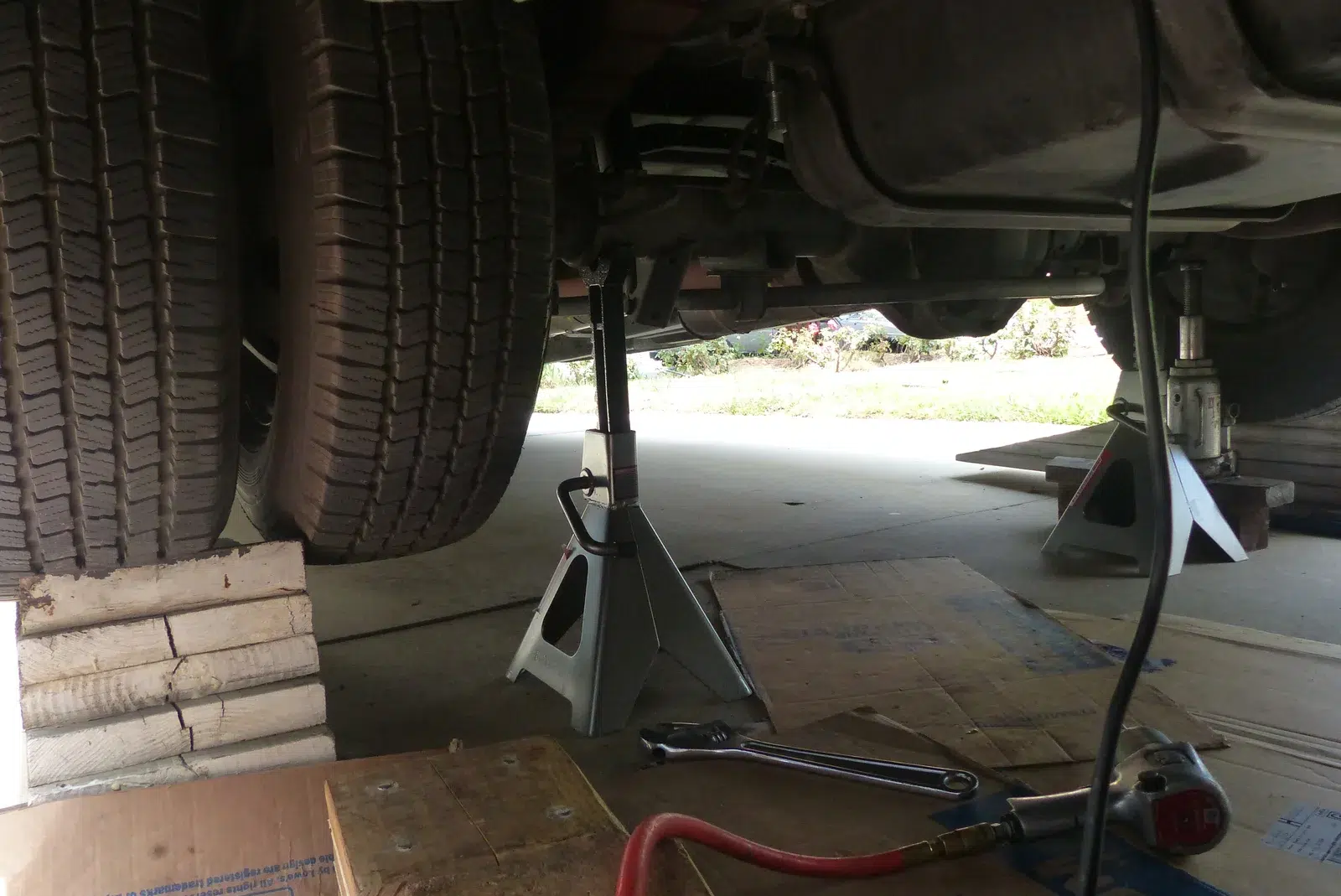 Ground-level view of a jack stand supporting a vehicle chassis rail with a trolley jack nearby