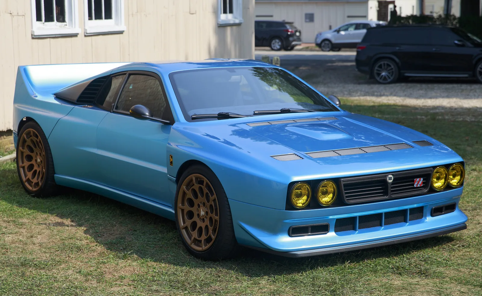 Pale blue Kimera EVO37 with yellow spotlights and bronze wheels, front three-quarter view on a lawn
