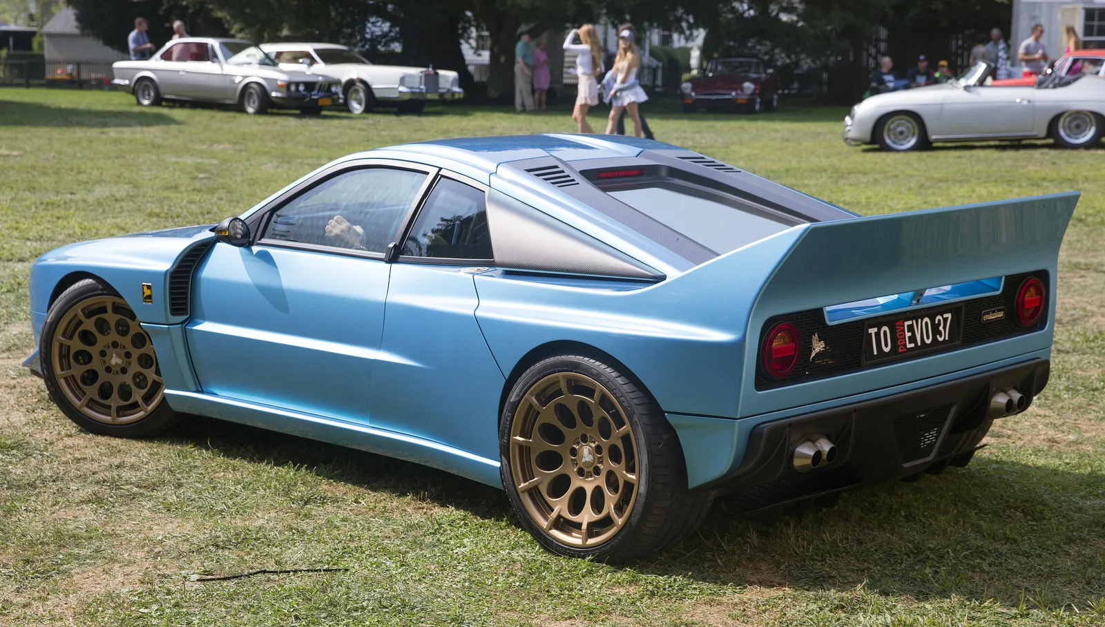 Rear three-quarter of a pale blue Kimera EVO37 showing its rear wing, round tail lights and twin exhausts
