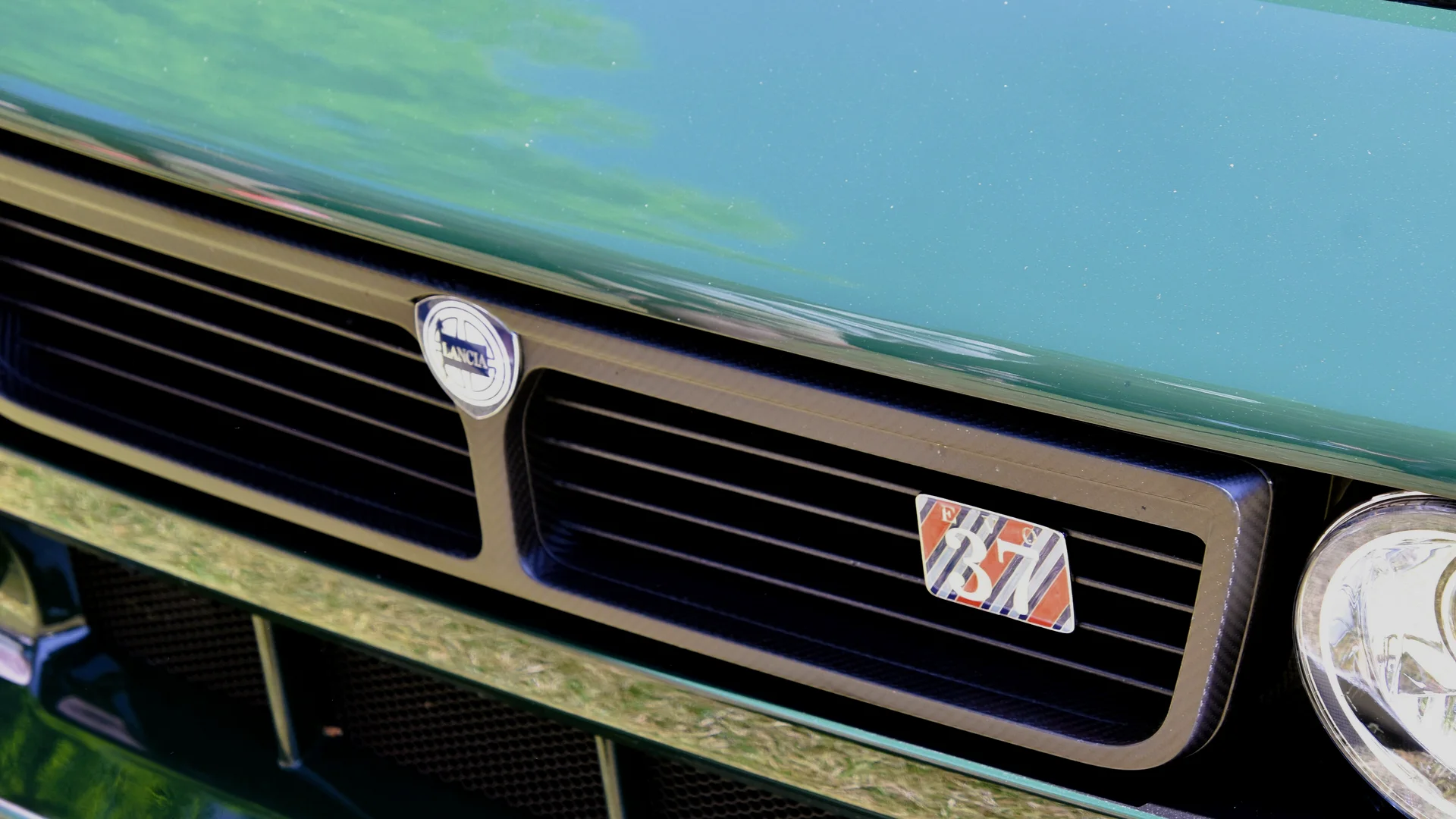 Close-up of a green Kimera EVO37's carbon fibre grille with the Lancia shield and enamel EVO 37 badge