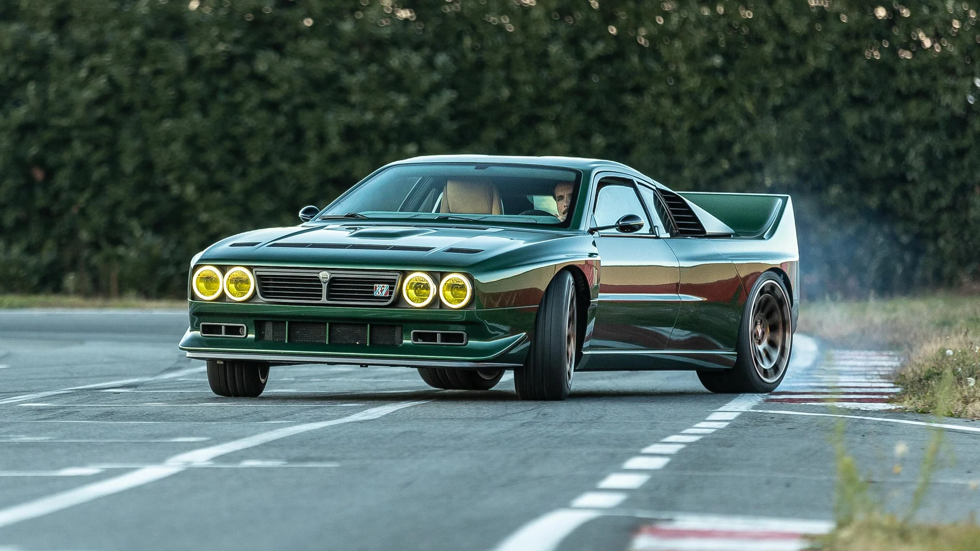 Kimera EVO37 cornering on a circuit Dark green Kimera EVO37 with yellow spotlights cornering over red and white kerbs on a race circuit
