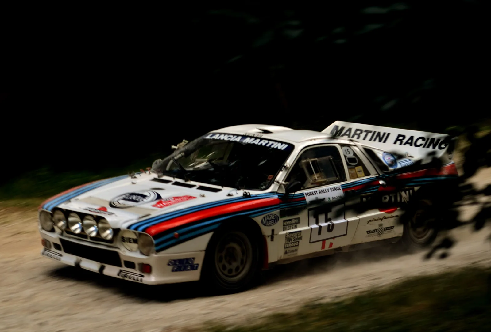 Martini-liveried Lancia Rally 037 Group B car kicking up gravel on the Goodwood Festival of Speed forest rally stage