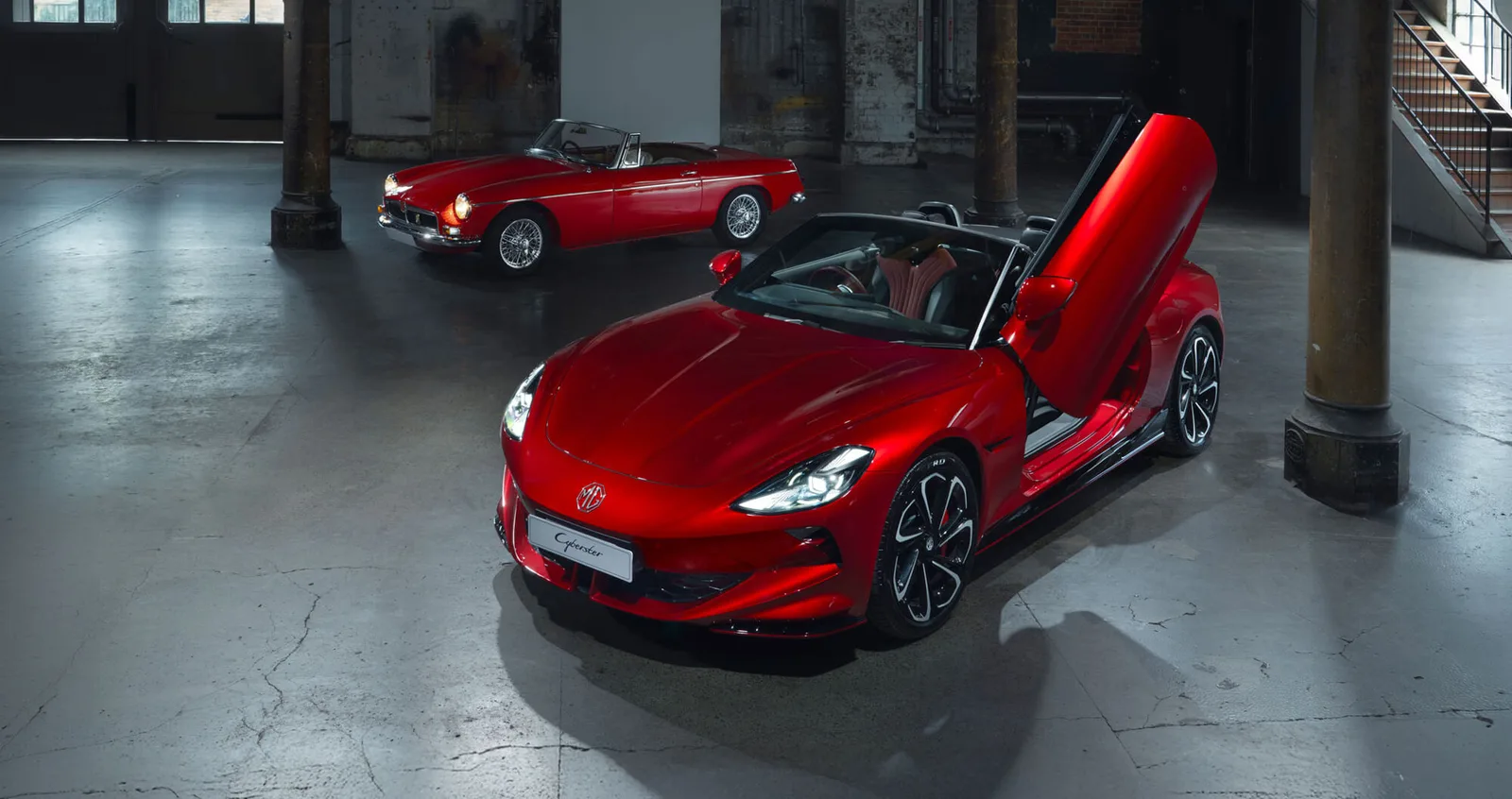 Red MG Cyberster with its scissor door raised in front of a classic red MGB roadster