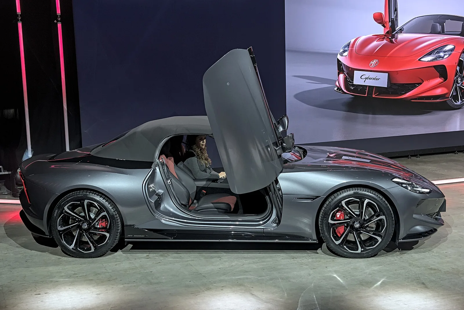 Grey MG Cyberster with fabric roof up and driver door raised, showing the long bonnet profile