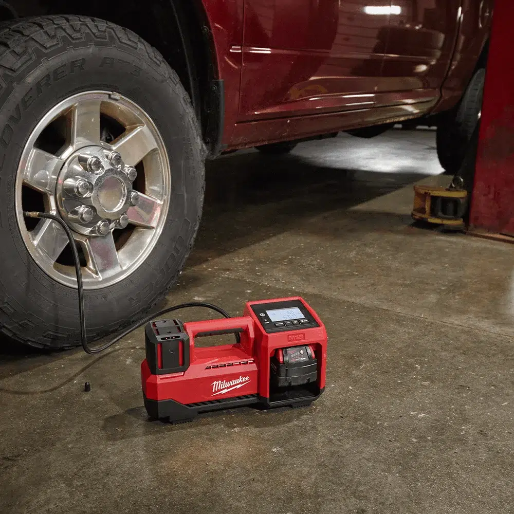 Milwaukee M18 cordless inflator connected to a car tyre on a garage floor, topping up pressure