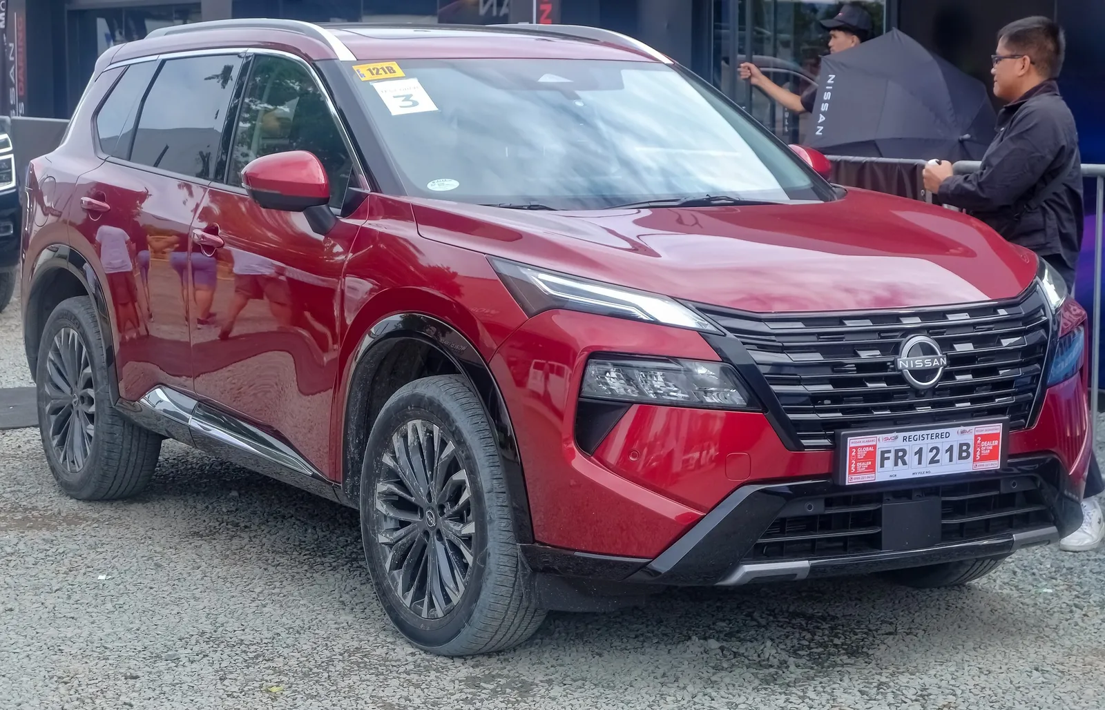 Red facelifted Nissan X-Trail e-Power on display at a motor show, front three-quarter view