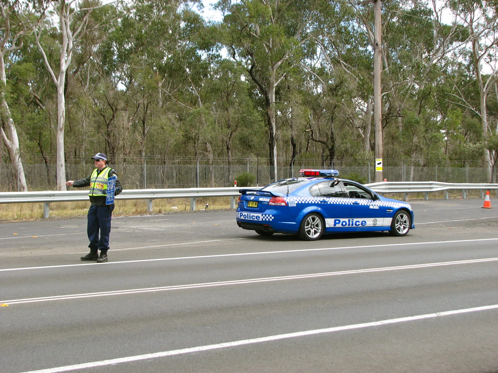 NSW Police Highway Patrol officer in hi-vis waving cars into a roadside check, with a patrol car behind