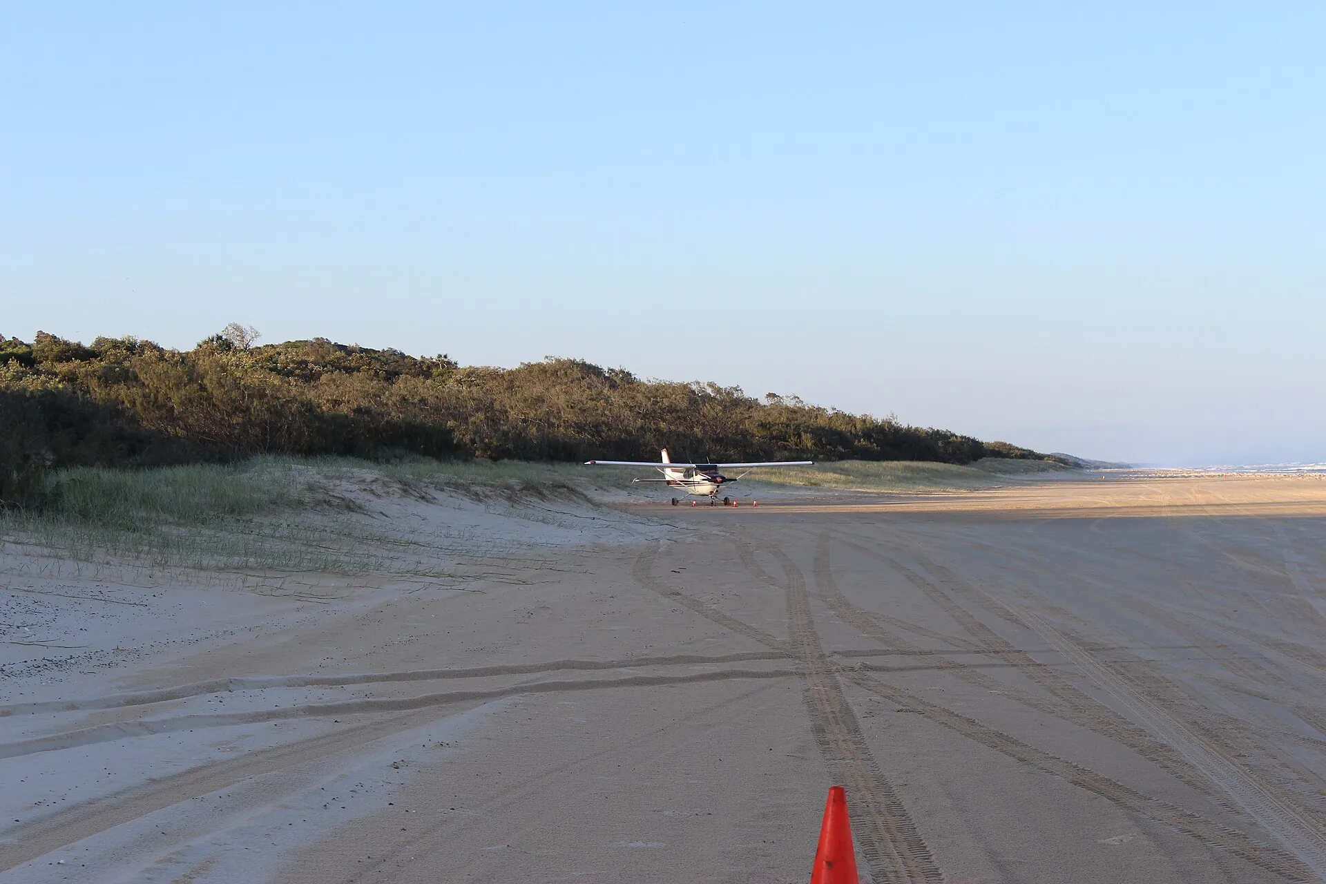 Light aircraft parked on a marked beach landing zone on K'gari's eastern beach with an orange cone and tyre tracks in front