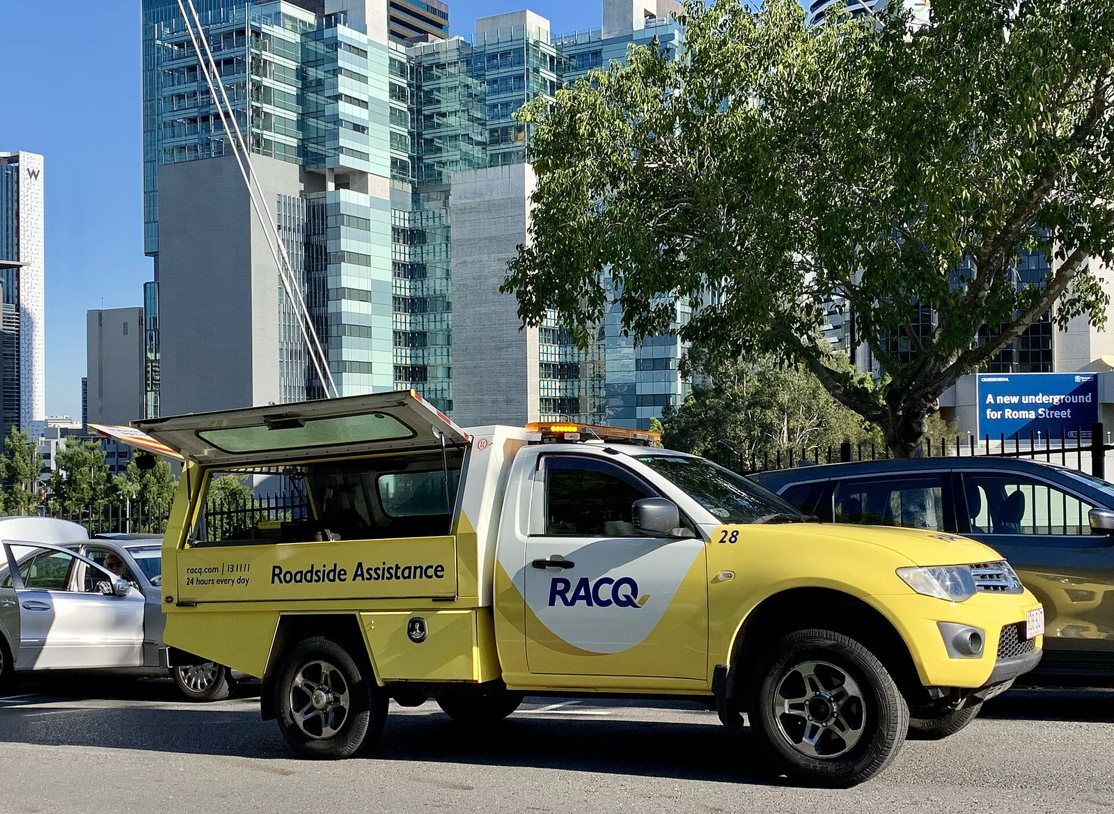 Yellow RACQ roadside assistance patrol ute attending a car on a city street in Brisbane