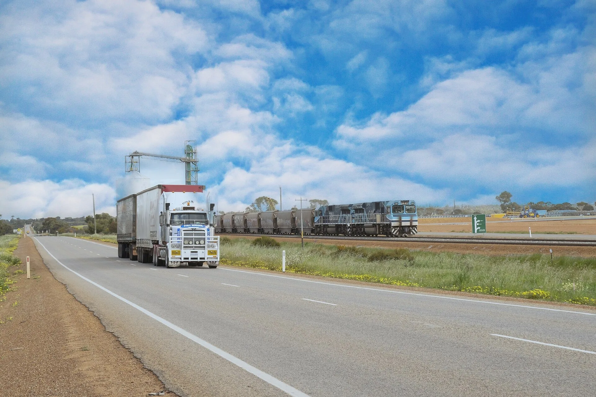 Road train heading along the Great Northern Highway near Dalwallinu in Western Australia beside a grain train
