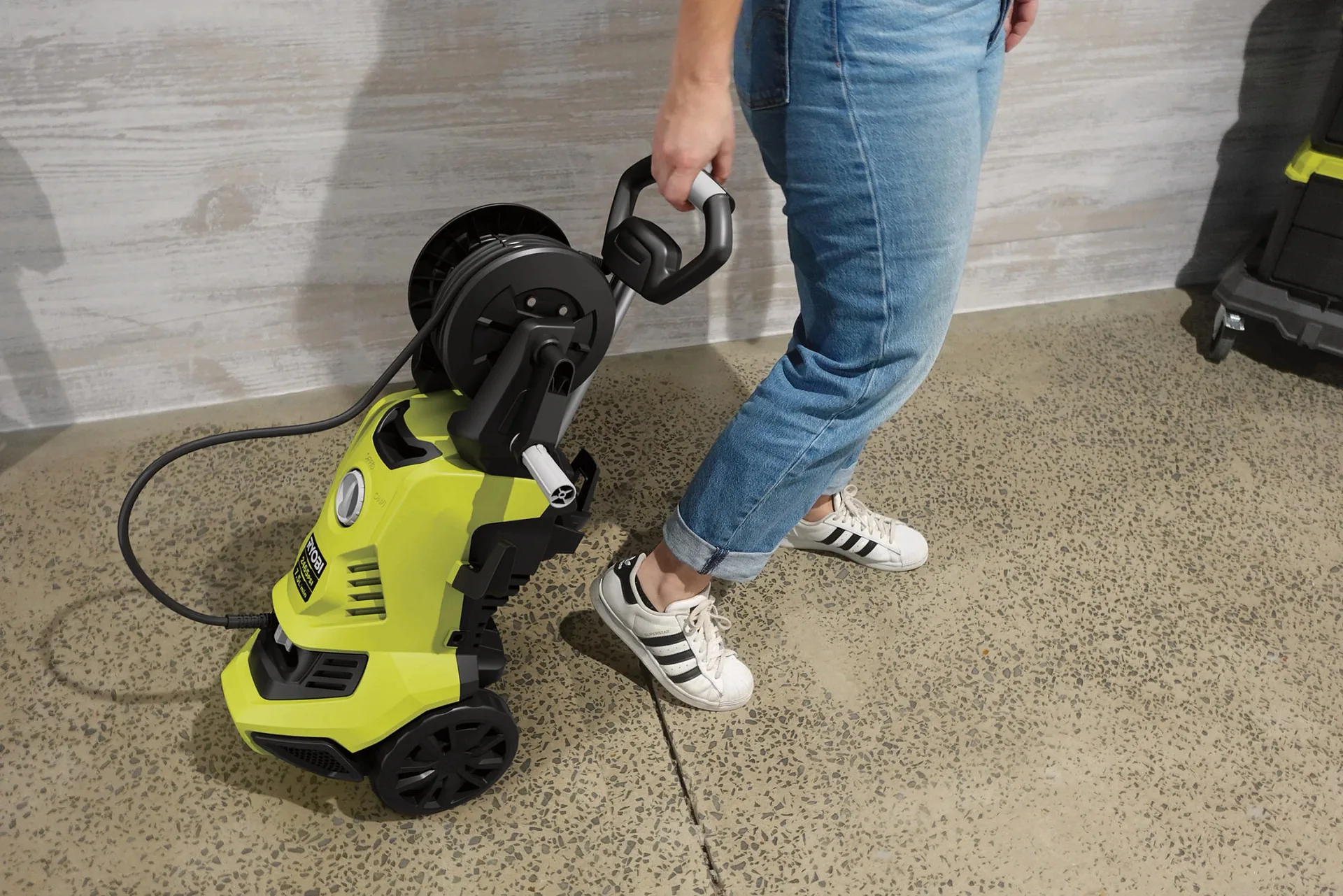 Ryobi 2465PSI RACPWS7 electric pressure washer with its hose reel being wheeled across a concrete floor
