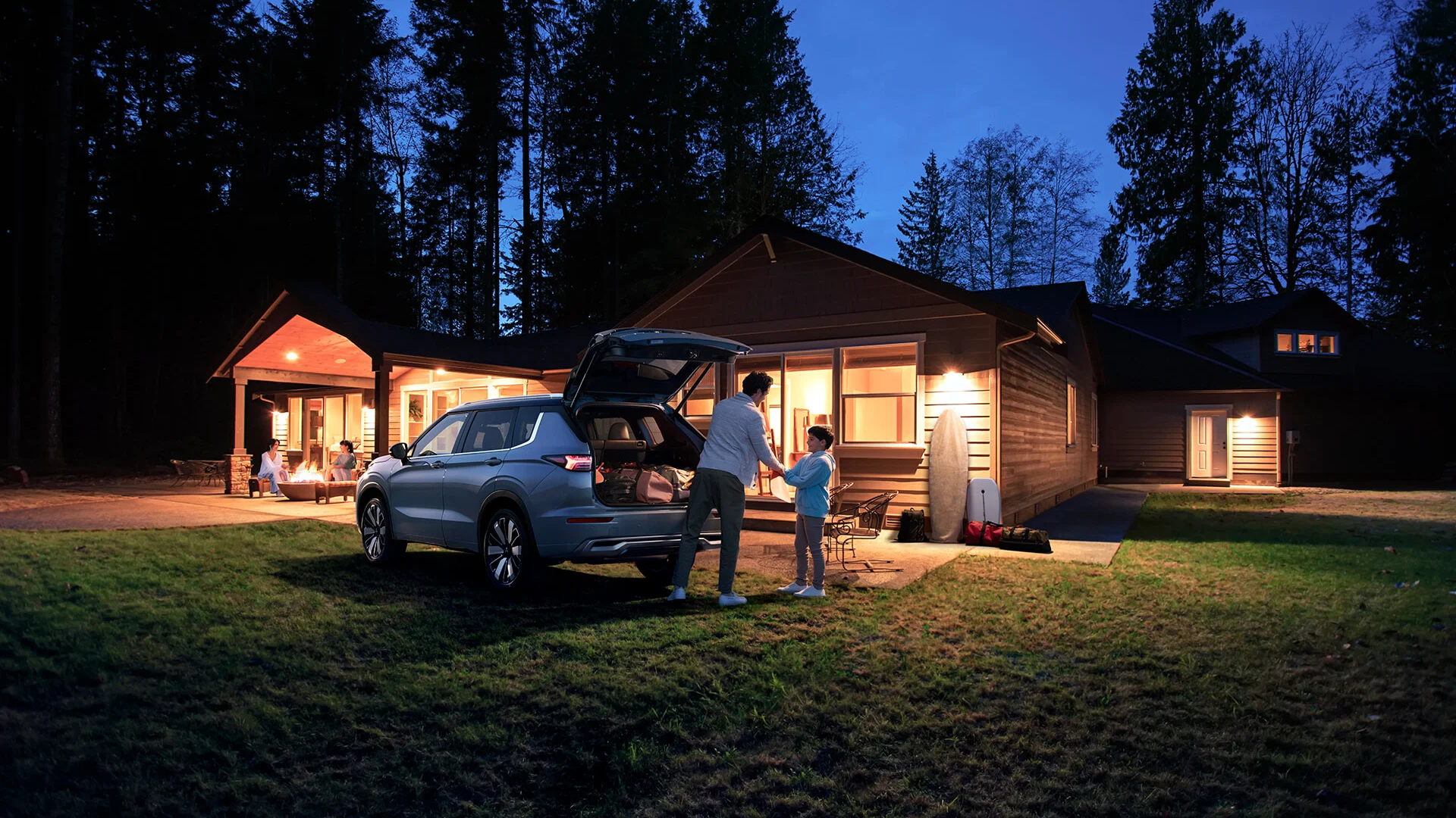 Family loading a seven-seat SUV at dusk Parent and young child at the open tailgate of a Mitsubishi Outlander seven-seat SUV outside a house at dusk