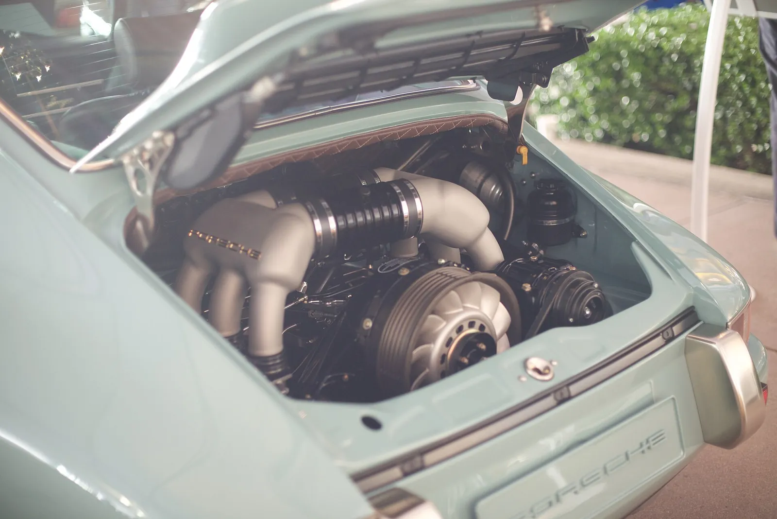 Air-cooled flat-six engine in the engine bay of a seafoam Singer 911 Classic, with quilted lining under the engine lid