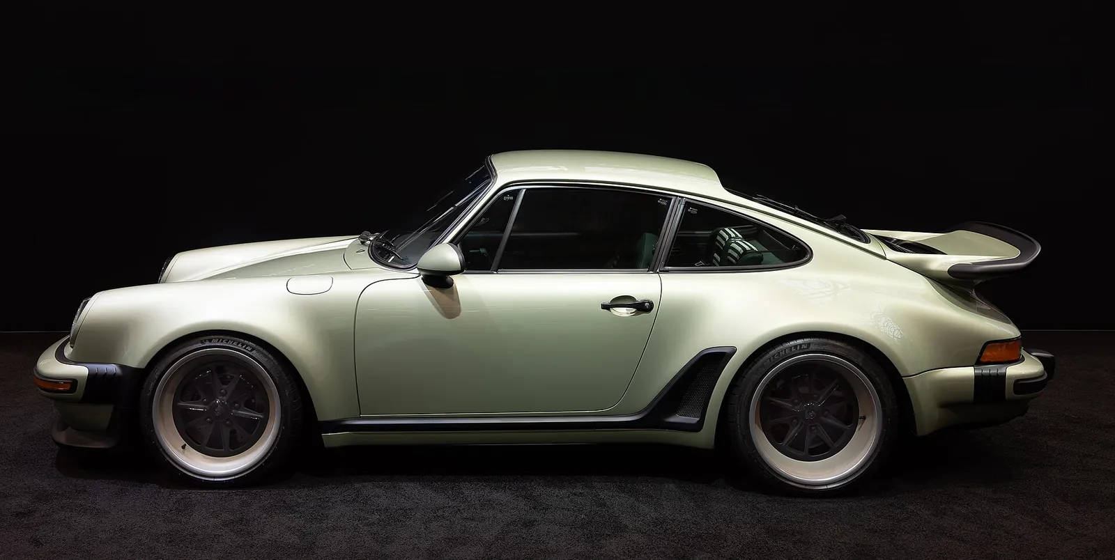 Full side profile of a silver Porsche 911 reimagined by Singer Classic Turbo with whale-tail spoiler against a black backdrop