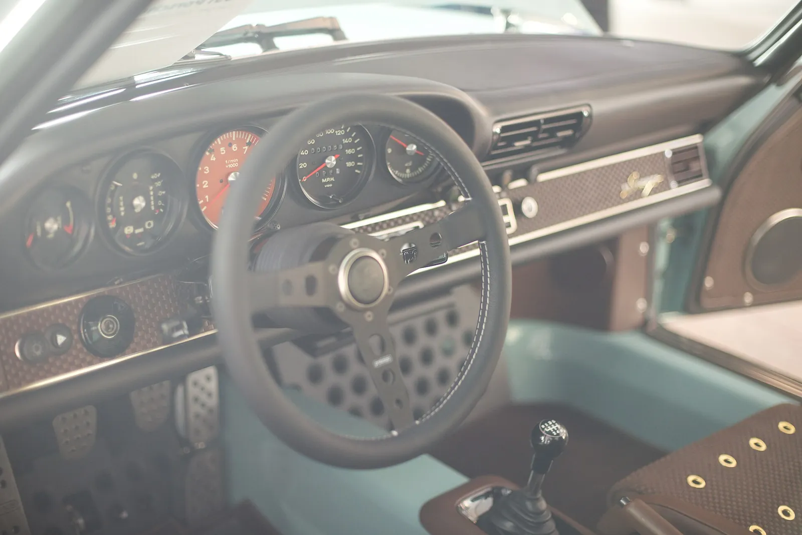 Five-dial instrument cluster with orange tachometer face, steering wheel and woven leather trim in a Singer 911