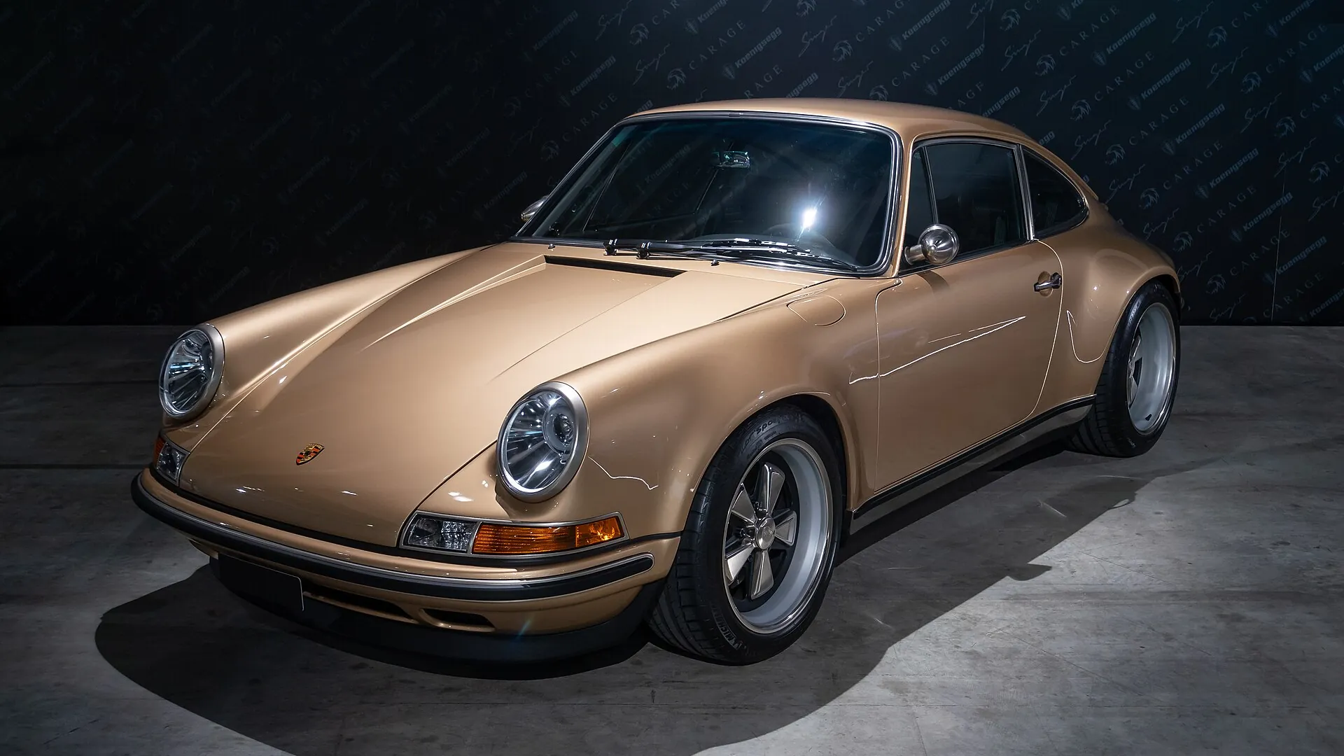 Porsche 911 Reimagined by Singer Bronze Porsche 911 Reimagined by Singer Classic on display against a dark backdrop, front three-quarter view