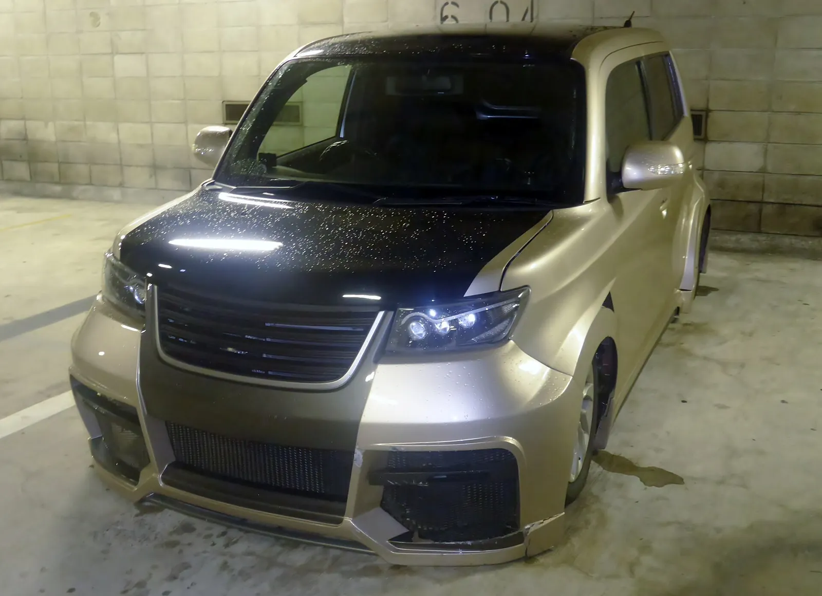 Slammed Toyota bB hatchback with its body almost touching the ground in a car park at night
