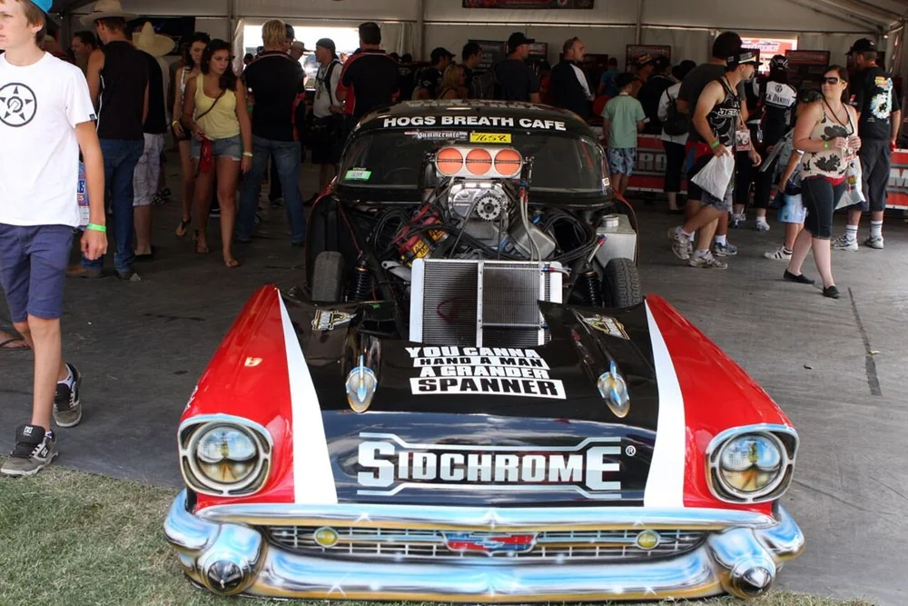 Supercharged airbrushed show car with chrome bumper on display under a marquee at Summernats as the crowd walks past
