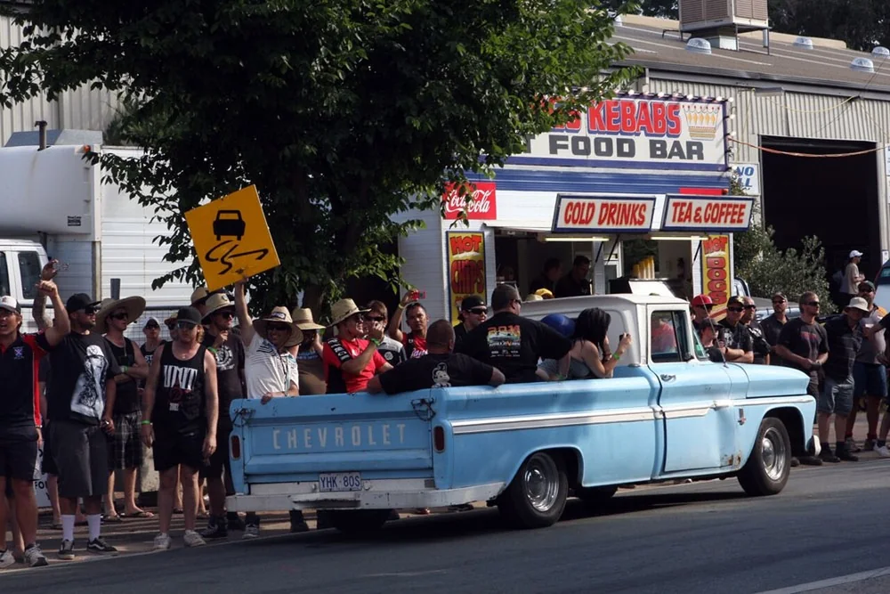 Pale blue 1960s Chevrolet pickup cruising past a packed crowd and food stalls on the Summernats cruise route