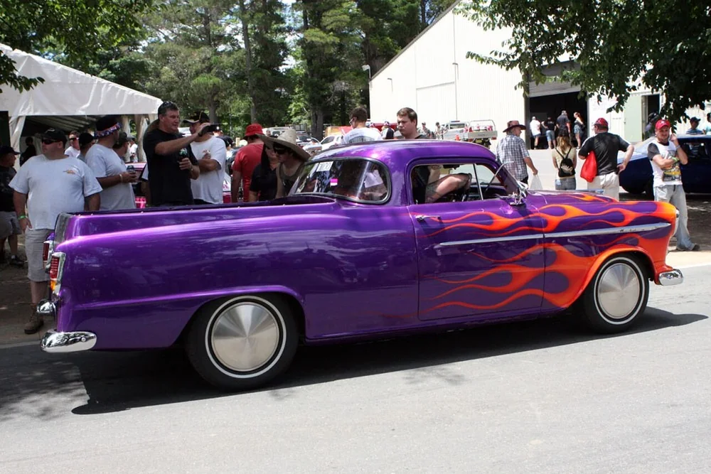 Purple Holden FE-era ute with orange flame paintwork and whitewall tyres cruising past the crowd at Summernats