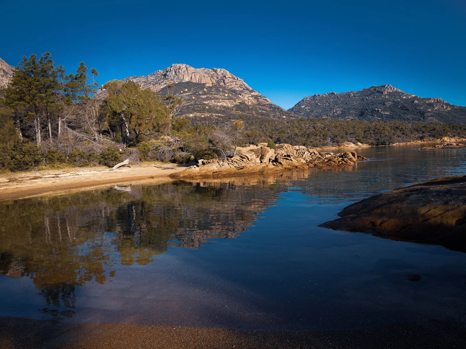 The pink granite peaks of The Hazards reflected in still water at Coles Bay, Freycinet National Park