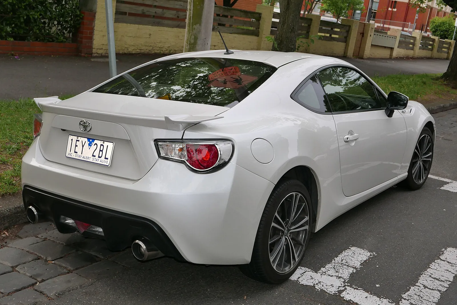 Rear three-quarter view of a white pre-facelift Toyota 86 GTS showing the boot spoiler, twin exhausts and tail-lights