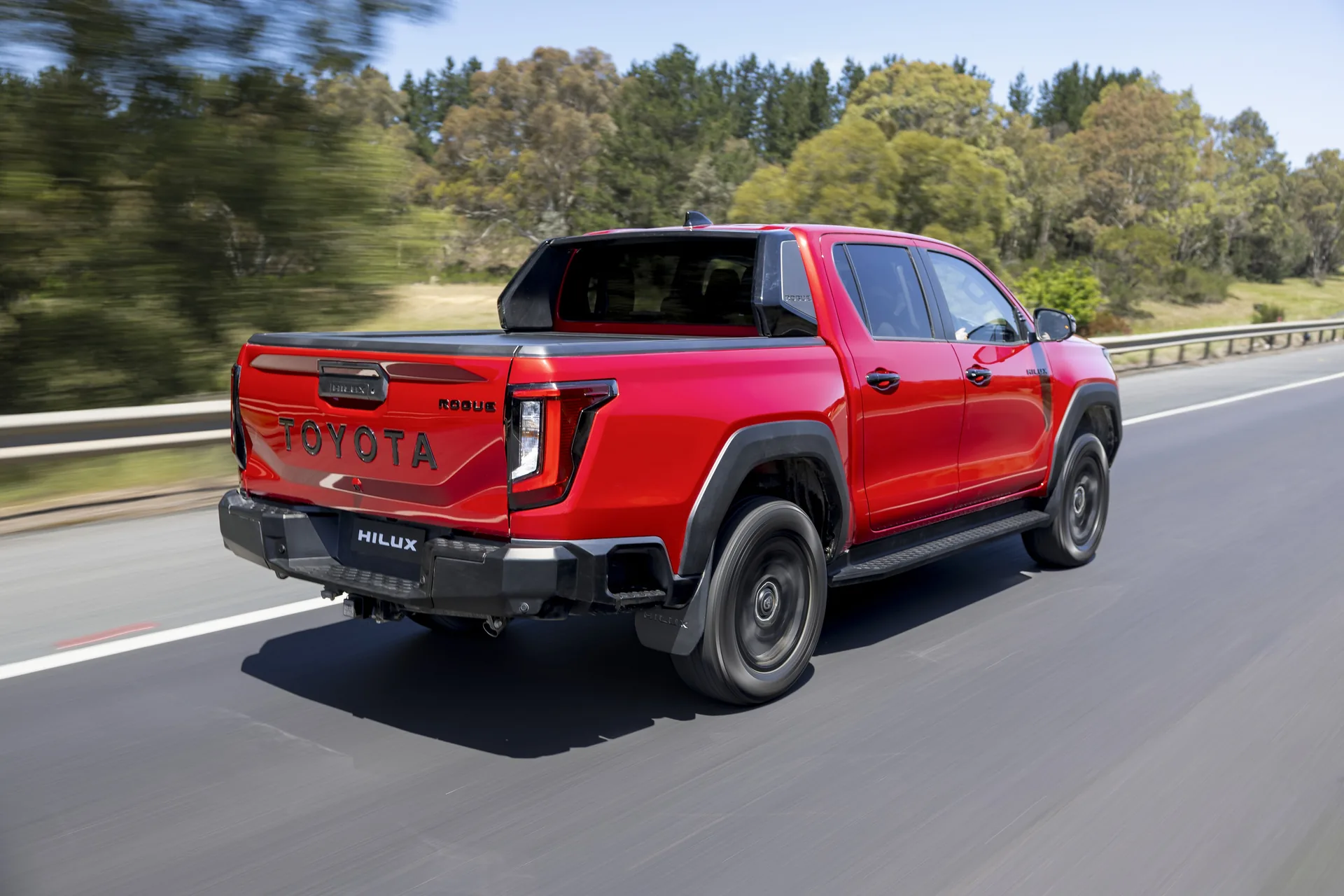 Red 2026 Toyota HiLux Rogue dual-cab ute driving on an Australian road, rear three-quarter view