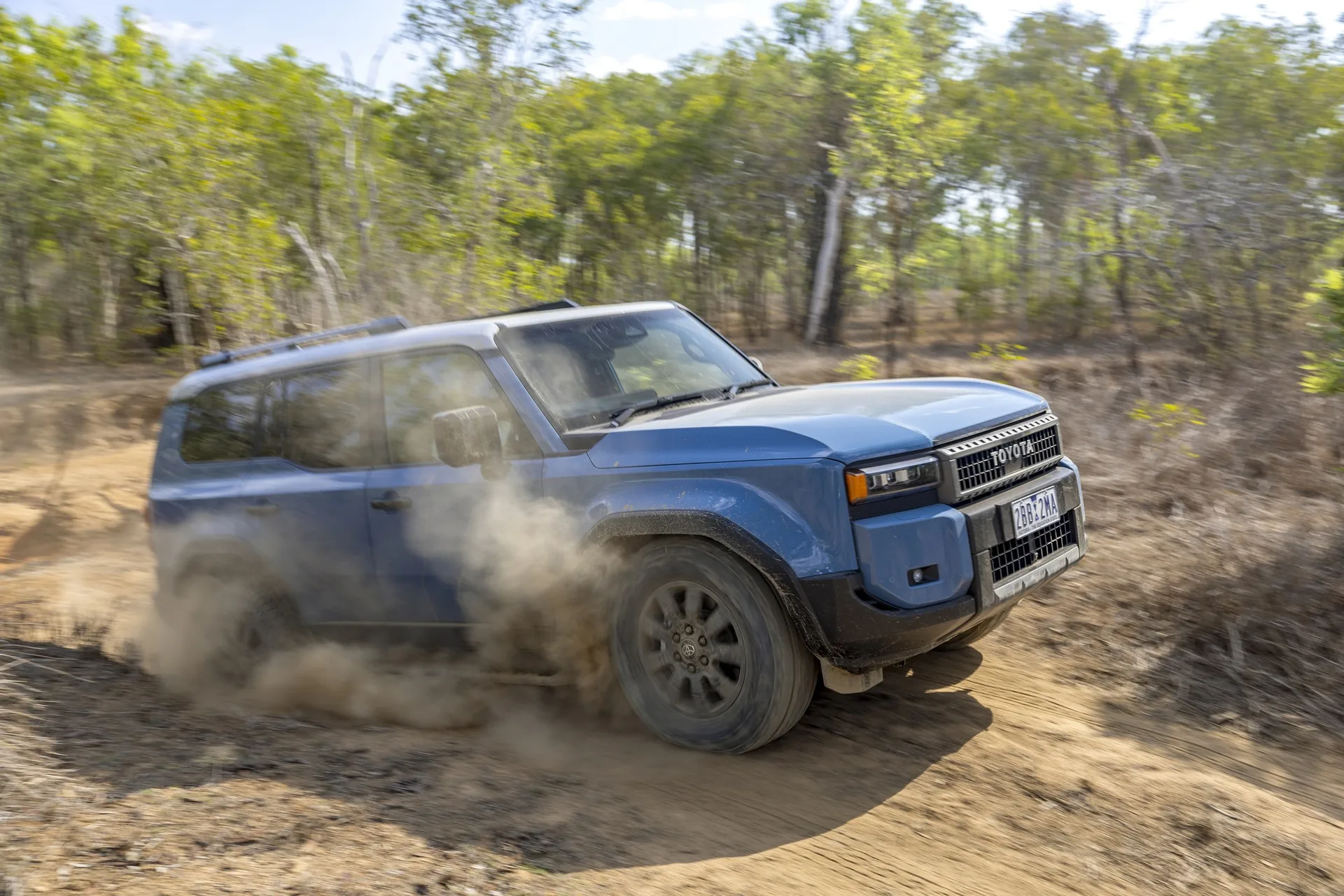Blue Toyota LandCruiser Prado Altitude kicking up dust on a dirt track through Australian scrub