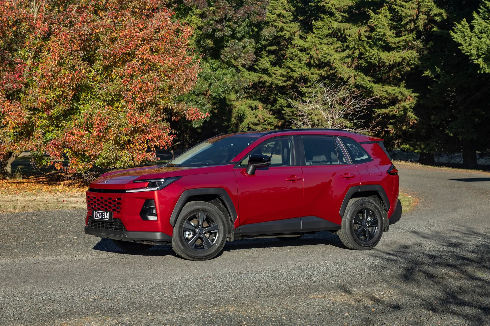 Red 2026 Toyota RAV4 Hybrid GX parked on gravel in front of autumn trees