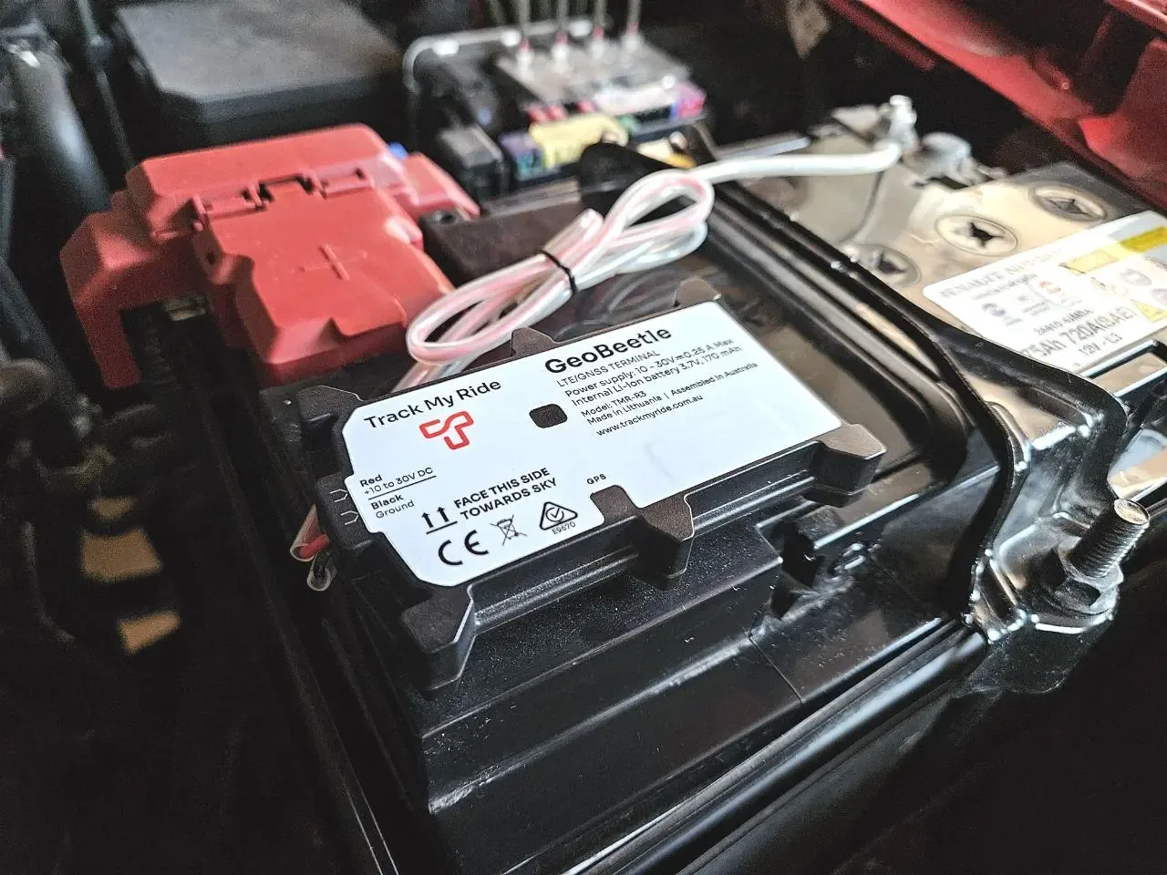 Track My Ride GeoBeetle wired GPS tracker mounted on top of a car battery under the bonnet