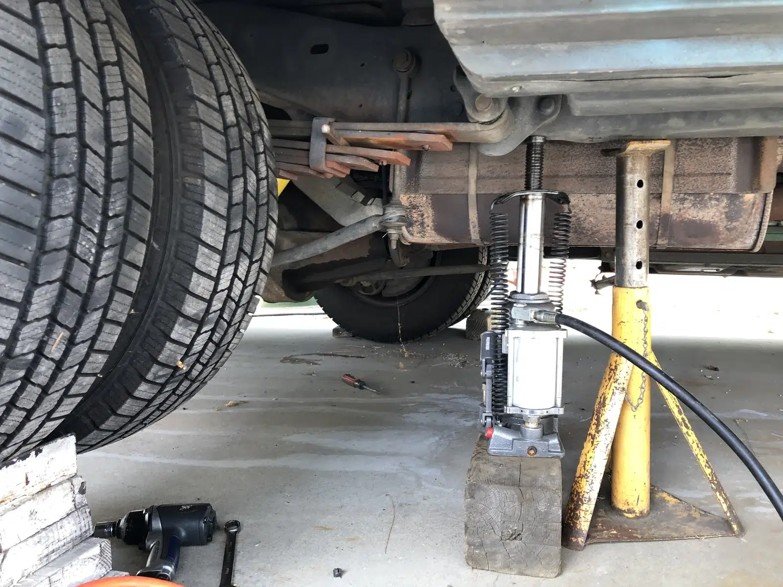 Trolley jack and a jack stand placed together under the sill of a raised car on a concrete floor