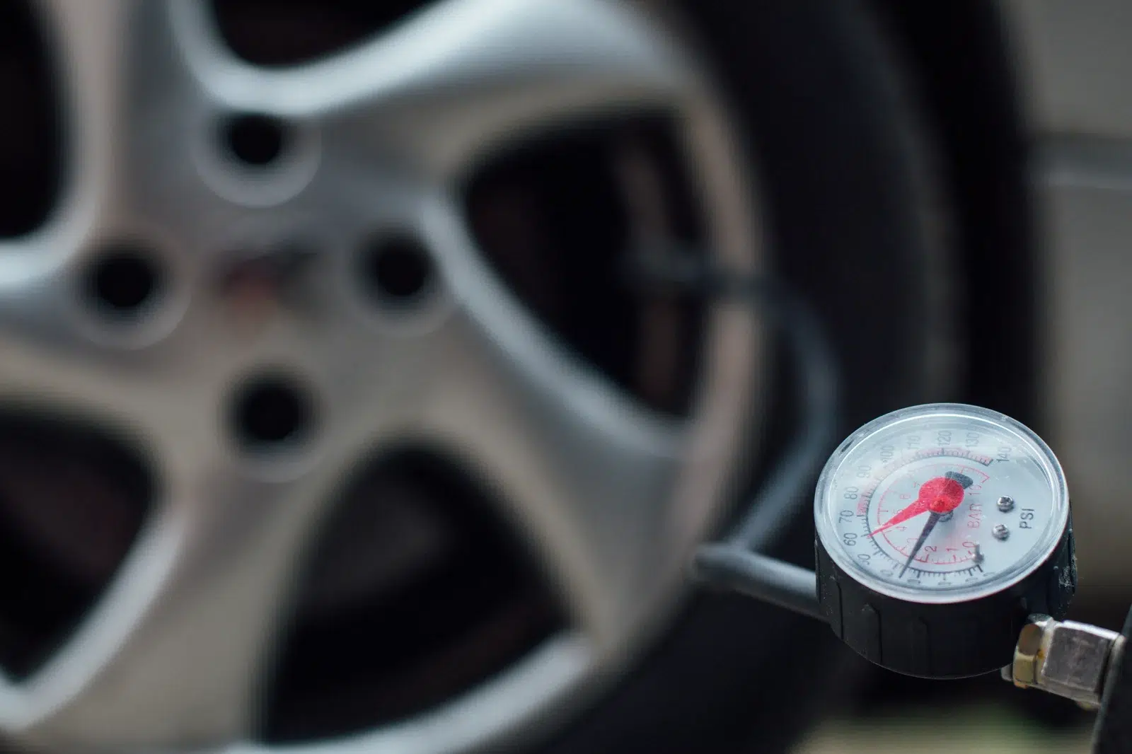 Close-up of a dial pressure gauge on an inflator hose with an alloy wheel behind it