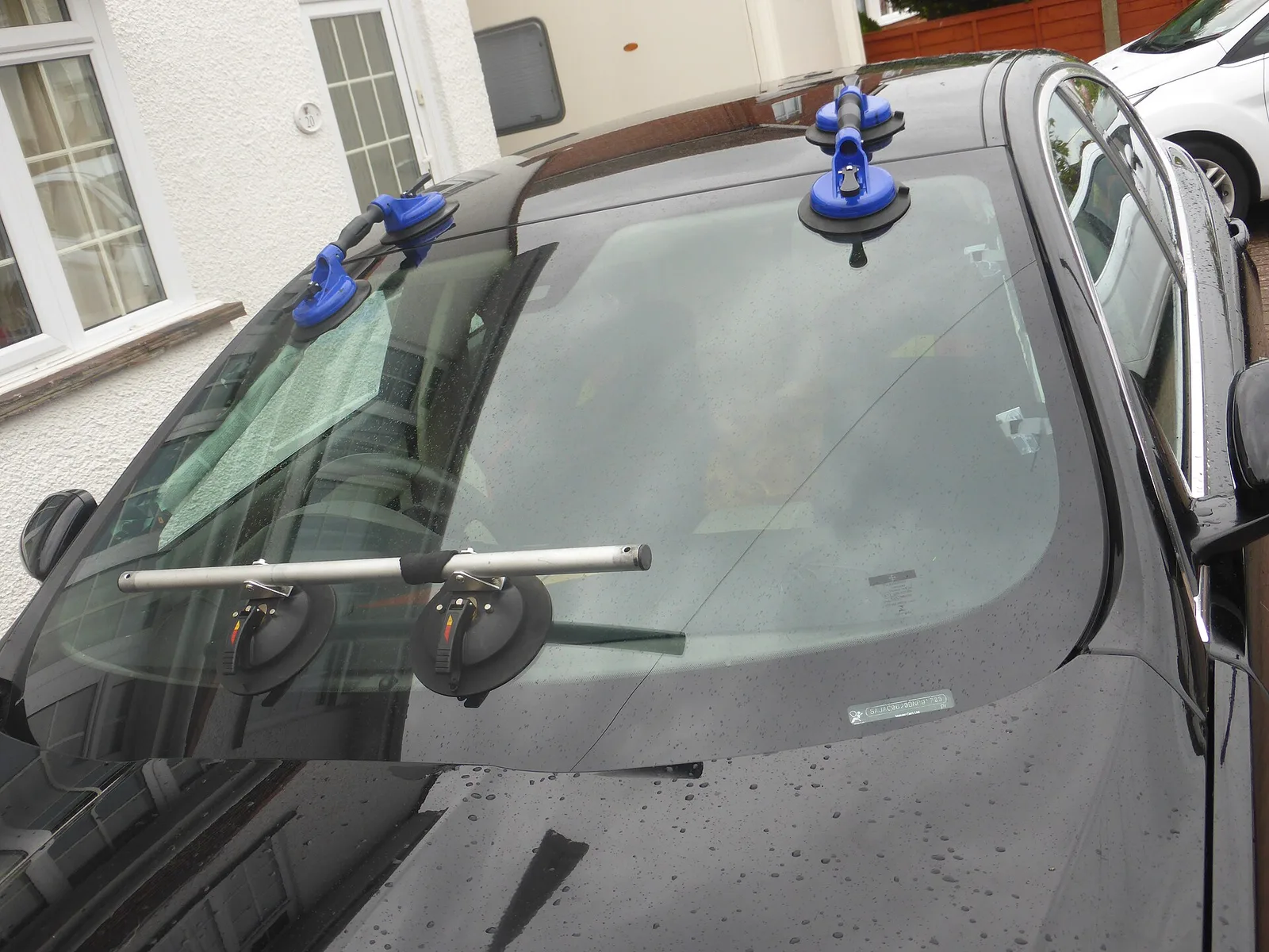 Replacement windscreen held in place with blue suction-cup lifters during fitting on a dark car